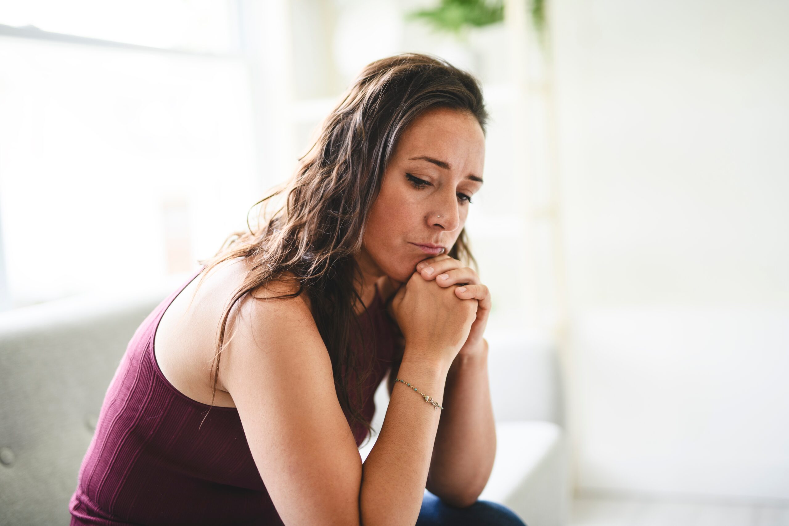 Woman in her early 40s sitting on the couch with a lonely, sad expression.
