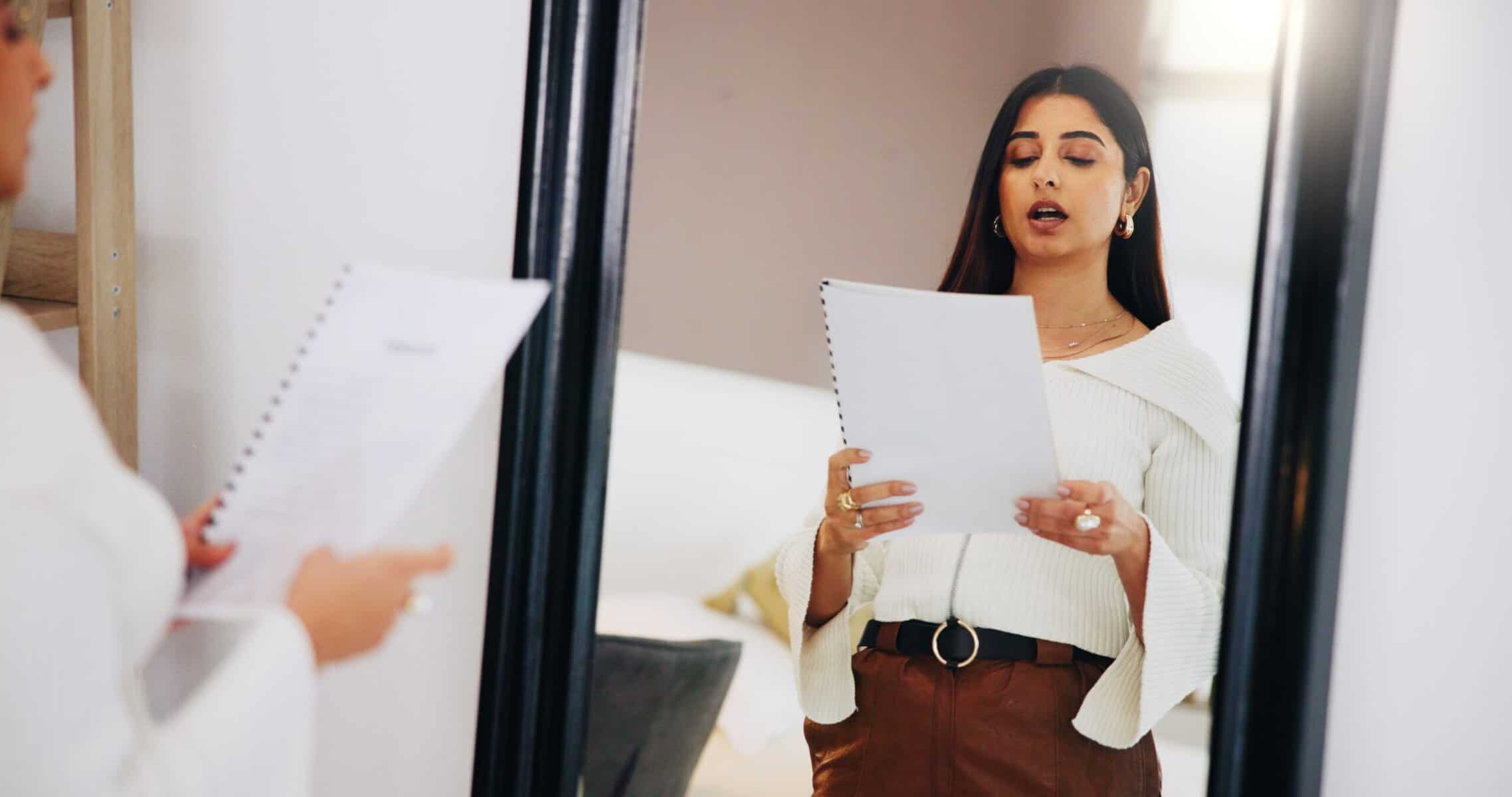 Nervous young woman rehearsing speech in front of a mirror.