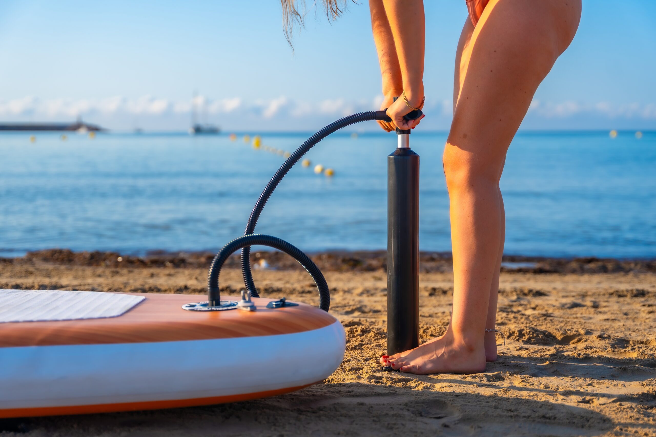 Woman inflating a paddle board on a sandy beach.