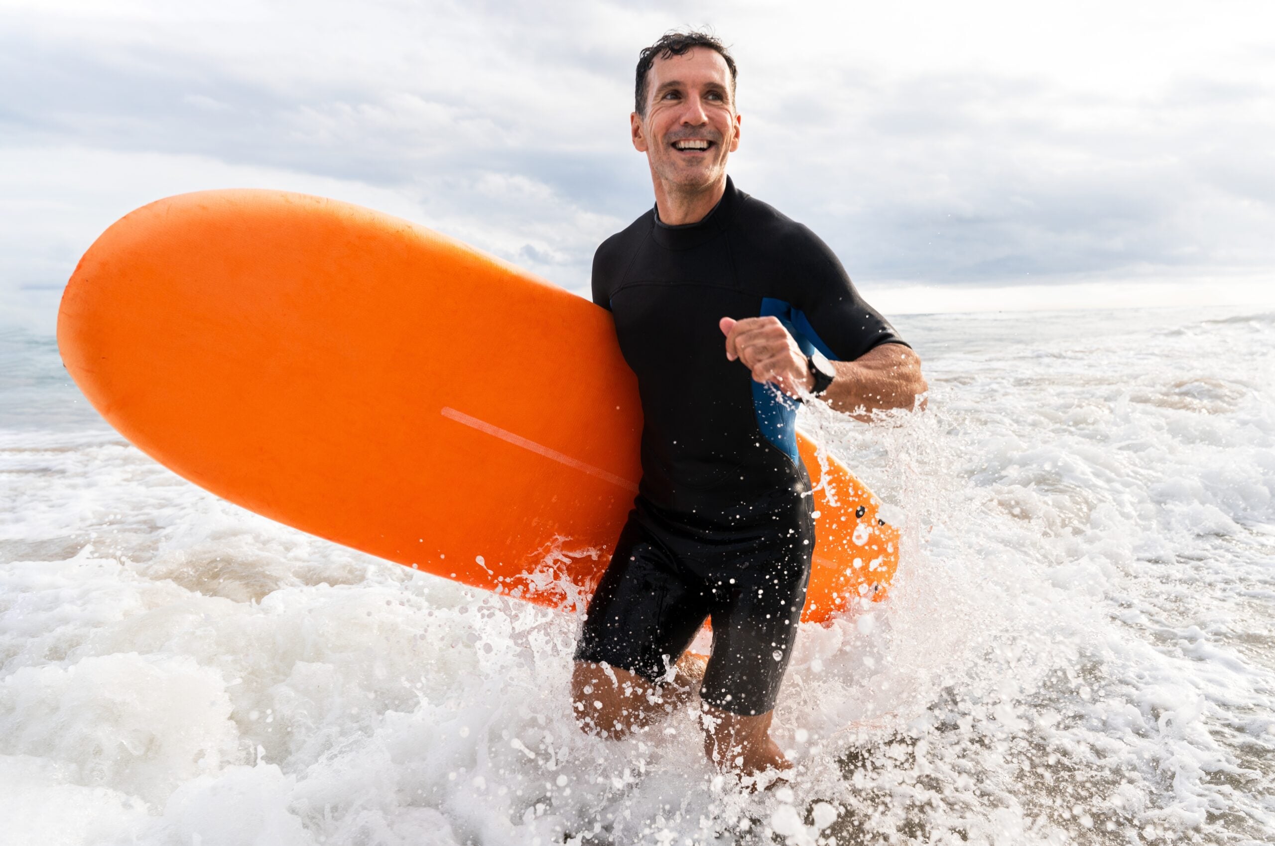 A single man at the ocean holding a bright orange surfboard.