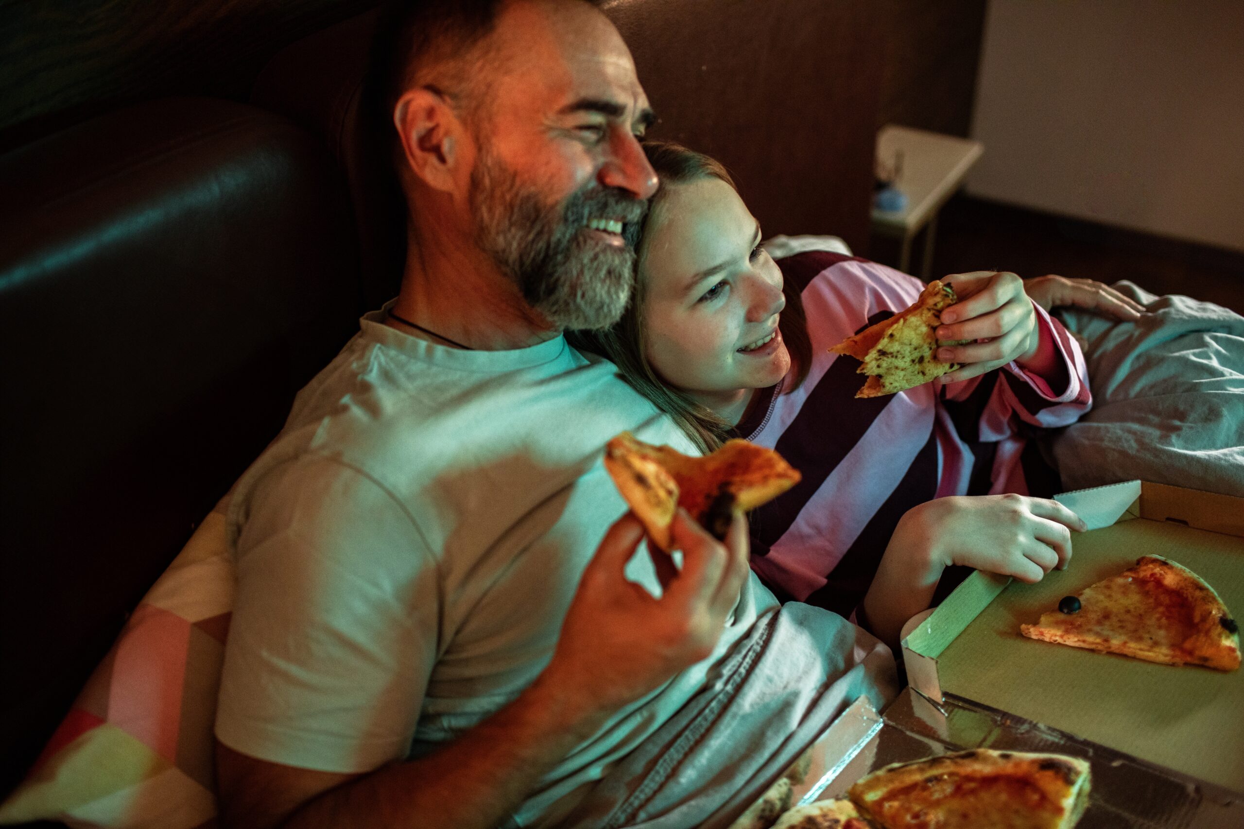 A father and daughter eating pizza and watching a movie together.