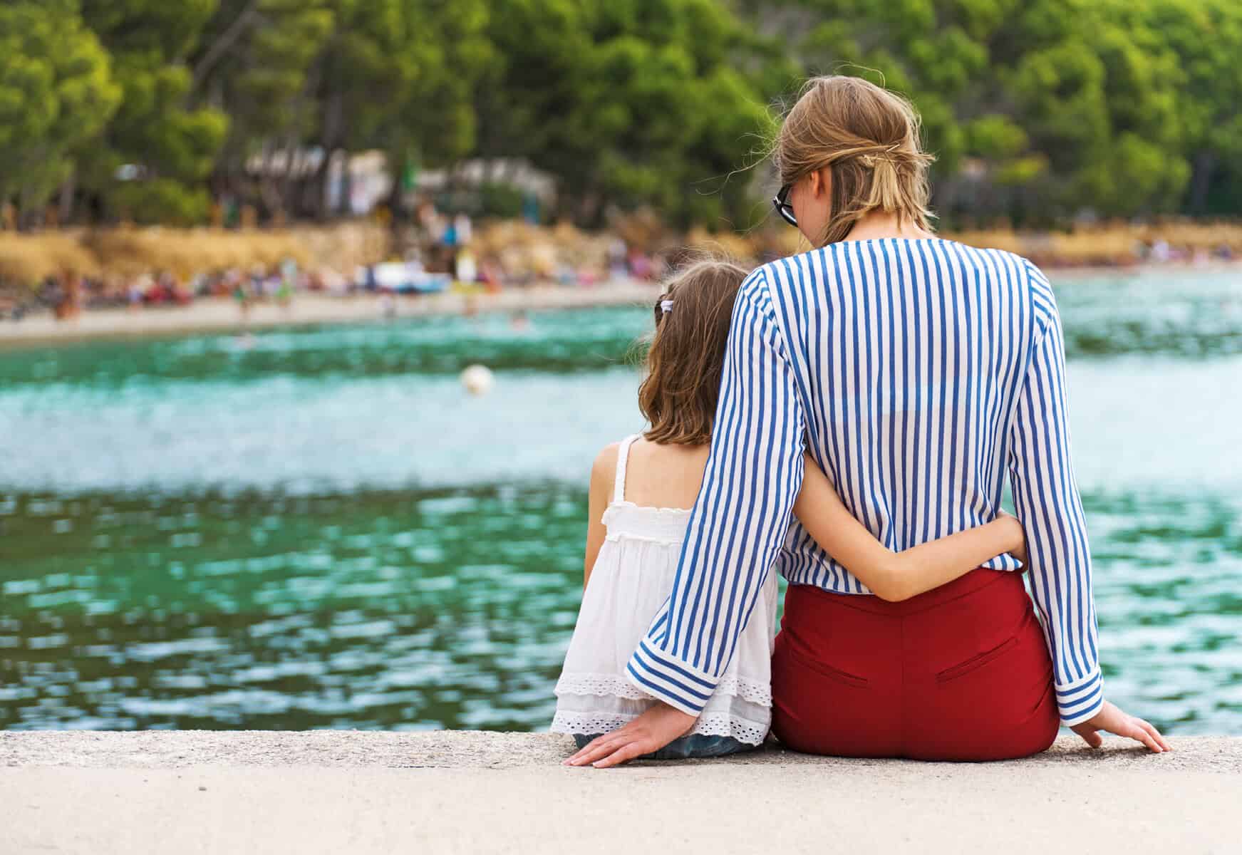 A small girl sitting poolside with her anxious mother.