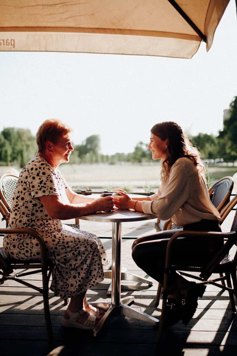 An elderly woman and young woman enjoying a sunny day at an outdoor café.