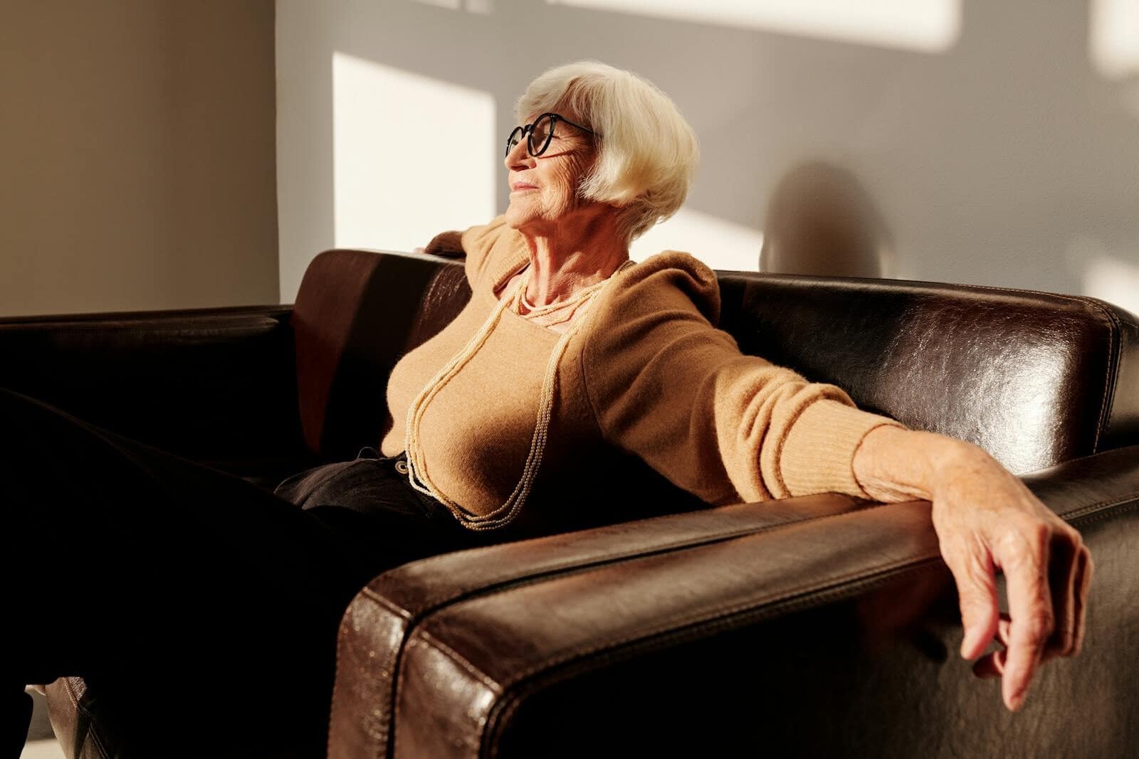 Senior woman with eyeglasses relaxing in a sunlit armchair indoors.