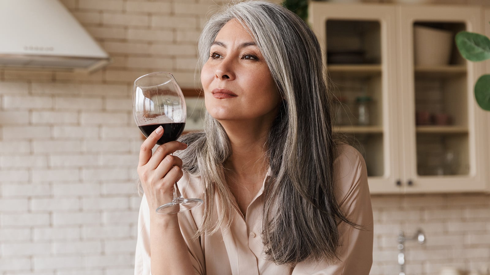 Picture of mature pretty woman sitting at the kitchen indoors at home drinking wine