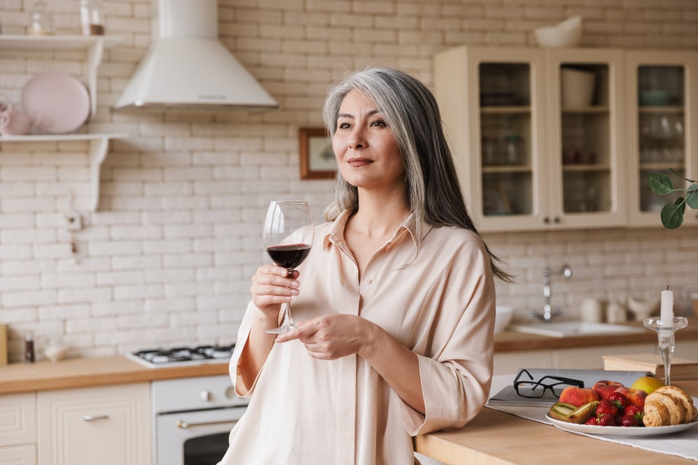 Picture of mature amazing pretty woman at the kitchen indoors at home drinking wine