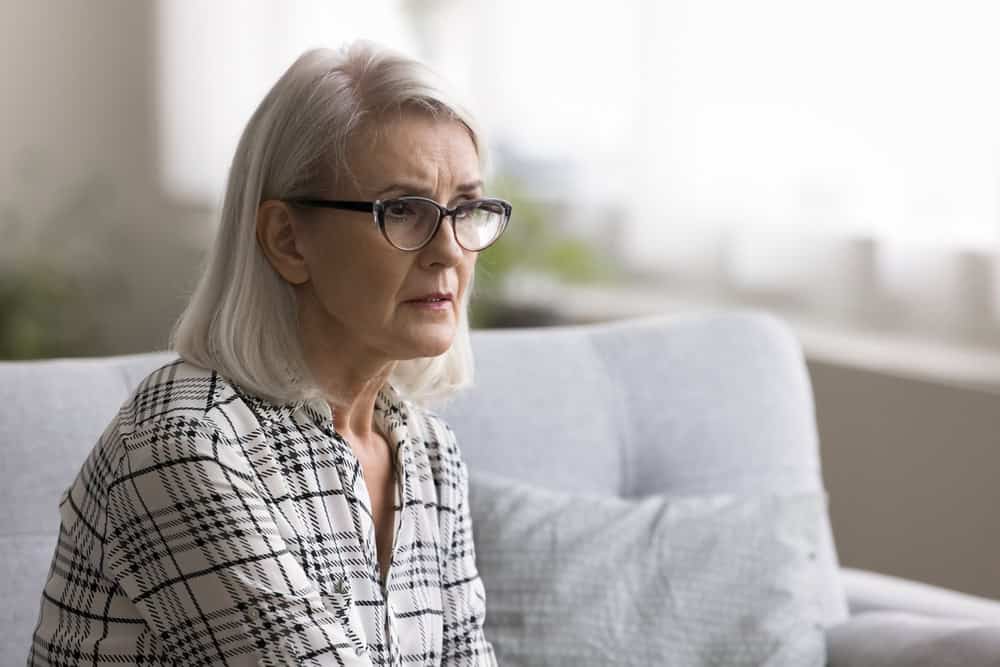 Reflective older woman, sorrowful sitting on couch