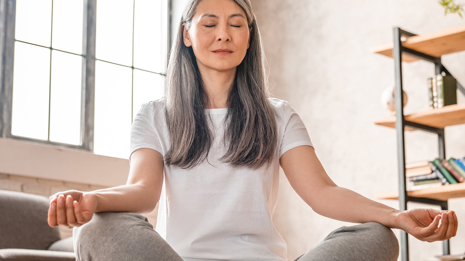 Grey-haired mature caucasian woman meditating at home