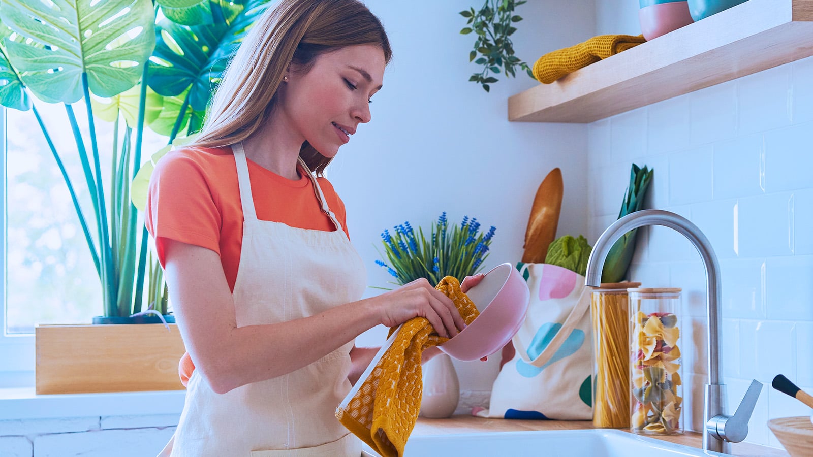 Beautiful young woman dries dishes at the domestic kitchen