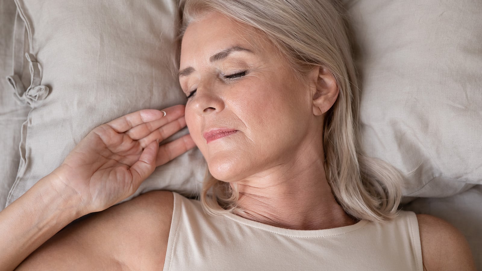 Peaceful beautiful mature woman sleeping in bed in the morning close up, relaxed older female with closed eyes lying on soft pillow top view, resting in bedroom, enjoying fresh bedclothes