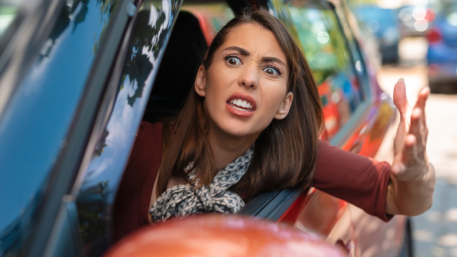 A woman sitting in a car with the window down looks frustrated and gestures angrily with her hand while looking outside, as if arguing or expressing road rage.