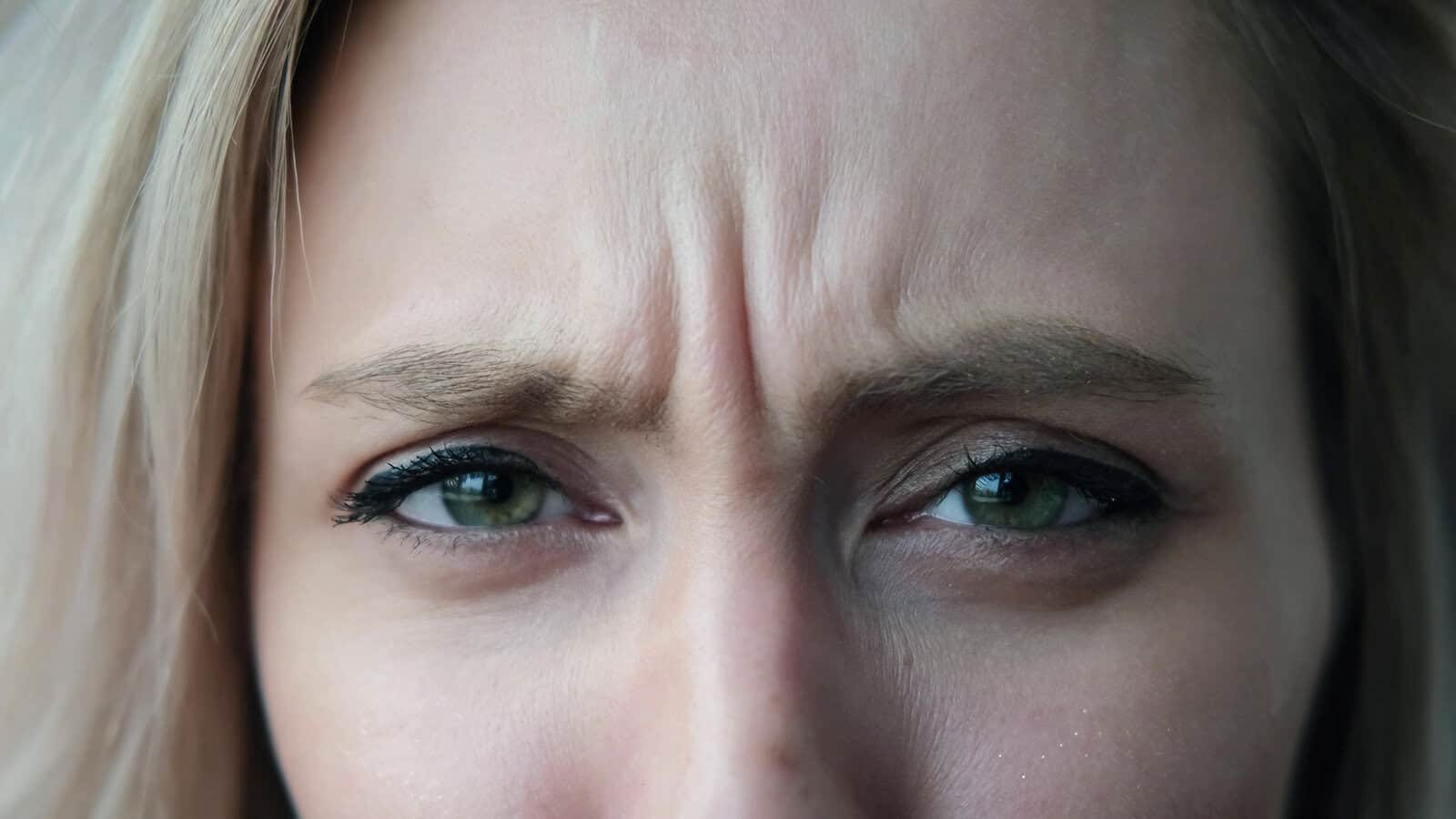 Close-up of a persons face showing green eyes and furrowed brows, suggesting concentration, confusion, or concern.