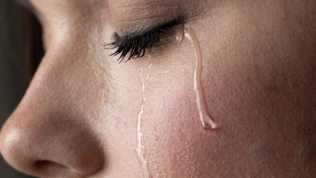 Close-up of a person’s face with closed eye and long eyelashes, showing two tears streaming down their cheek—a powerful depiction of grief and mourning.