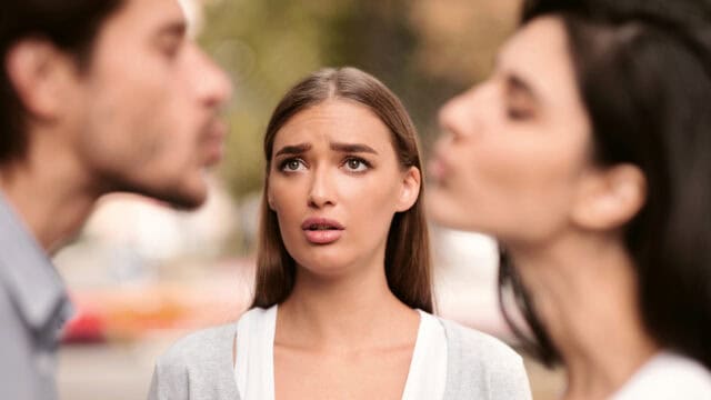 A woman looks concerned as two people, a man and a woman, lean in toward each other as if to kiss, with their faces out of focus in the foreground—an evocative scene that highlights the psychology of jealousy in relationships.