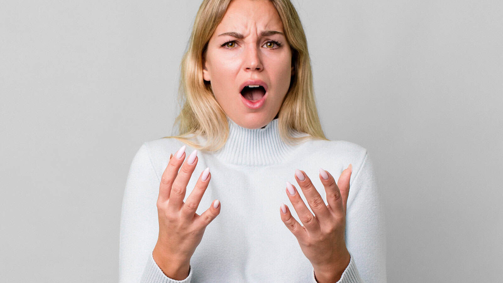 A woman with long blonde hair wearing a white sweater looks surprised or upset, possibly experiencing decision fatigue, with her mouth open and hands raised in front of her against a plain light background.