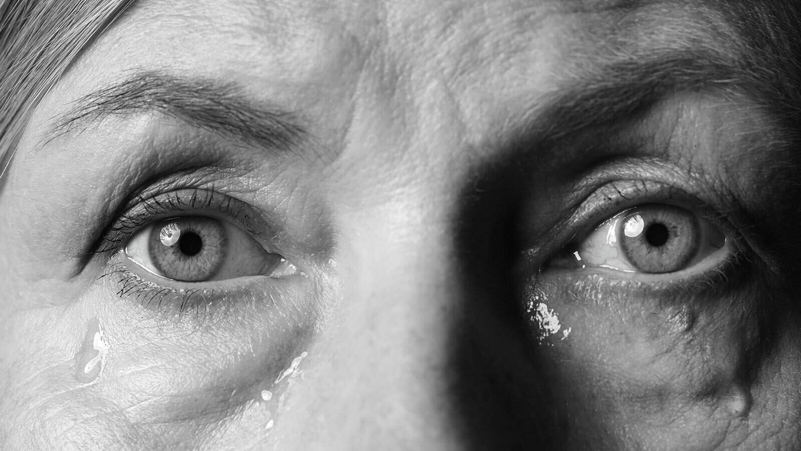 Close-up black and white photo of an older persons eyes with visible tears on their cheeks, showing detailed skin texture and emotional expression.