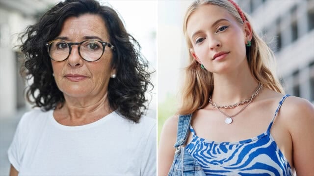 Two women outside: one older with curly dark hair, glasses, and a white shirt; the other younger with long blonde hair, a blue patterned top, and layered necklaces. Both face the camera with neutral expressions.