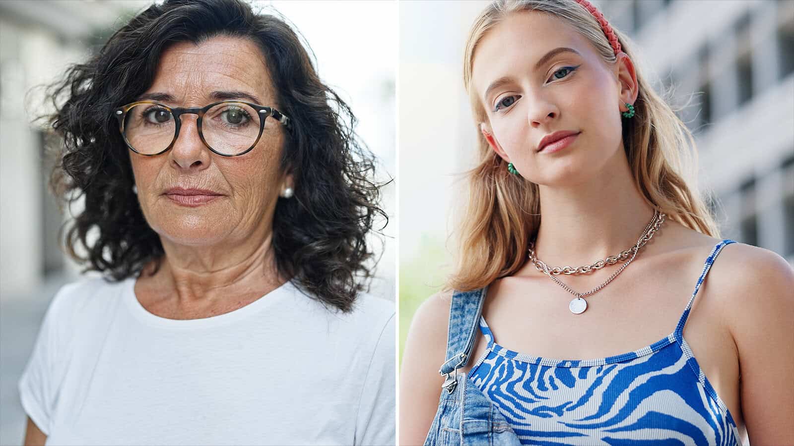 Two women outside: one older with curly dark hair, glasses, and a white shirt; the other younger with long blonde hair, a blue patterned top, and layered necklaces. Both face the camera with neutral expressions.