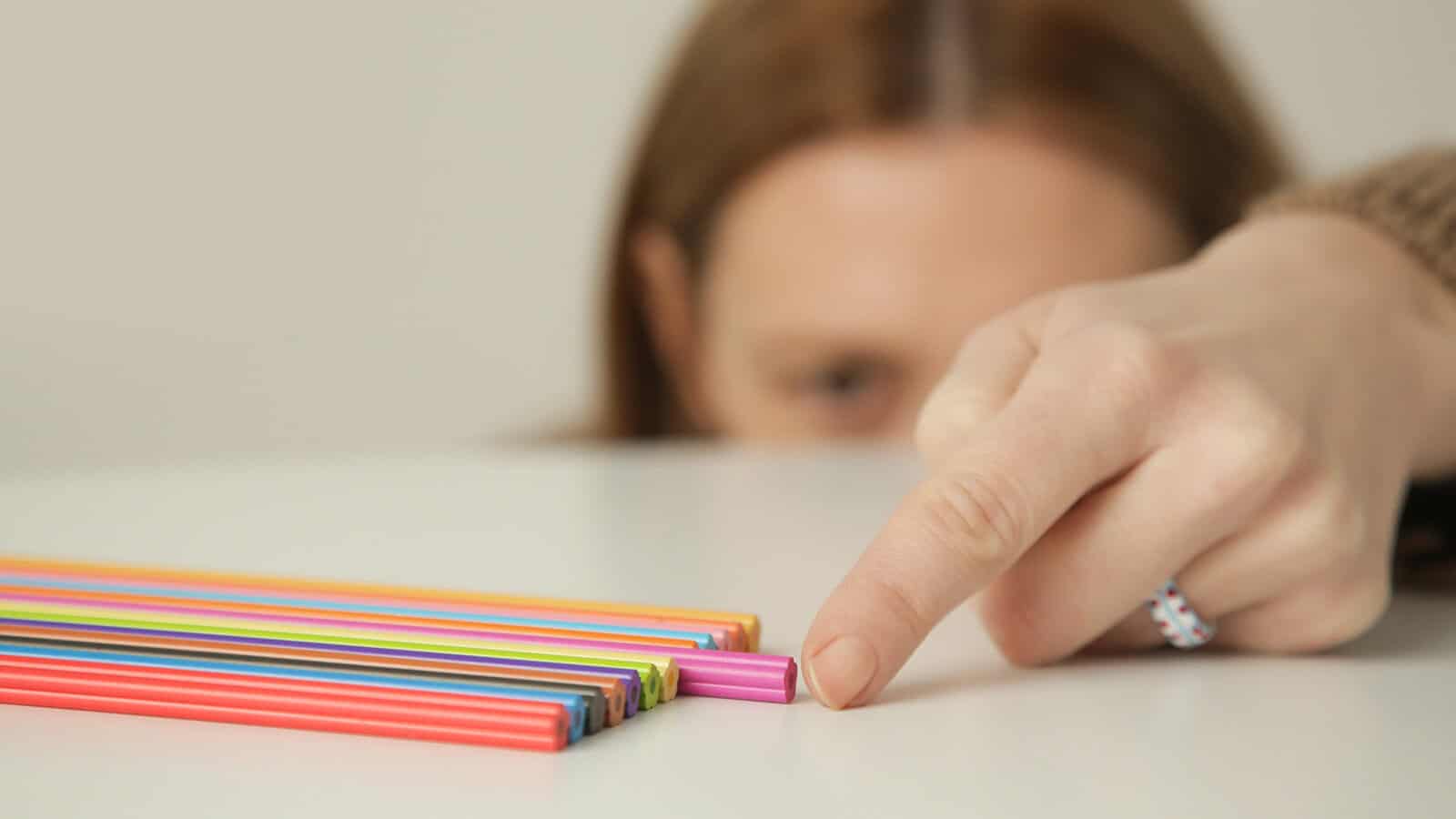 A person points at a pink straw slightly out of alignment with a neat row of colorful straws on a white surface.