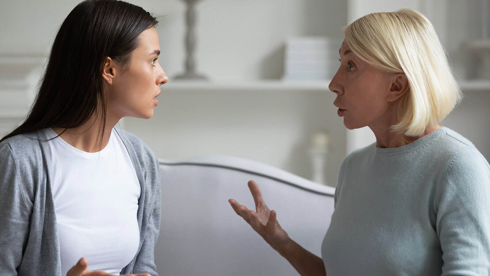 Two women sitting indoors on a couch are facing each other and appear to be having an intense or emotional conversation, with expressive hand gestures and serious facial expressions.