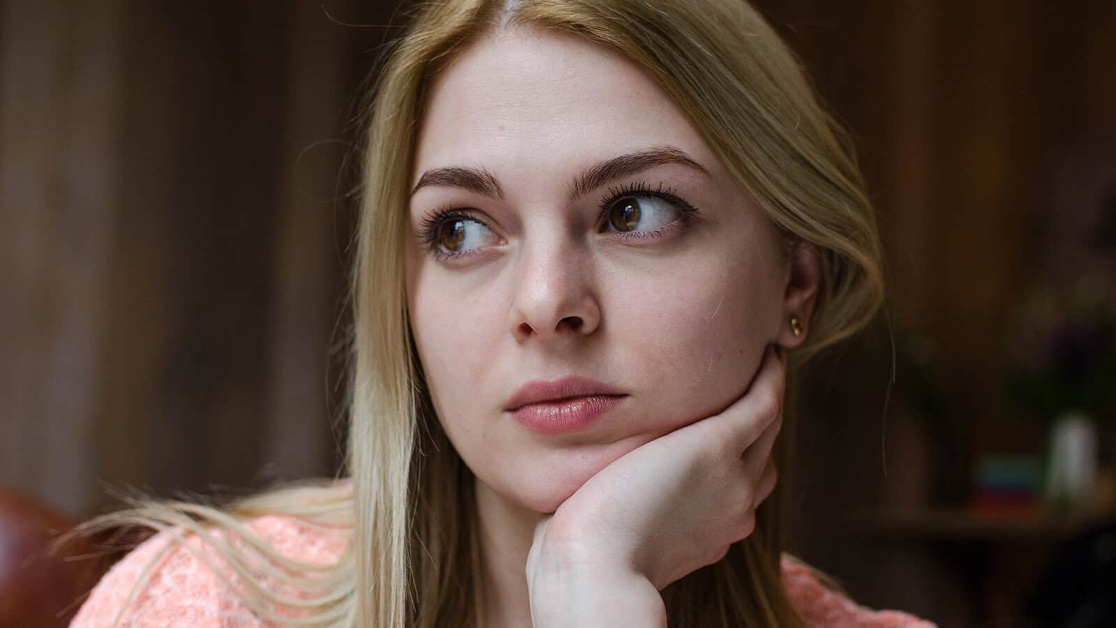 A young woman with blonde hair looking to the side with her hand resting on her chin.