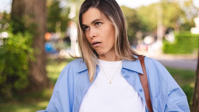 A woman in a blue shirt looks upward with a skeptical expression.