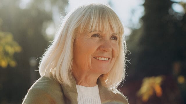 A smiling older woman with blonde hair looking away from the camera.