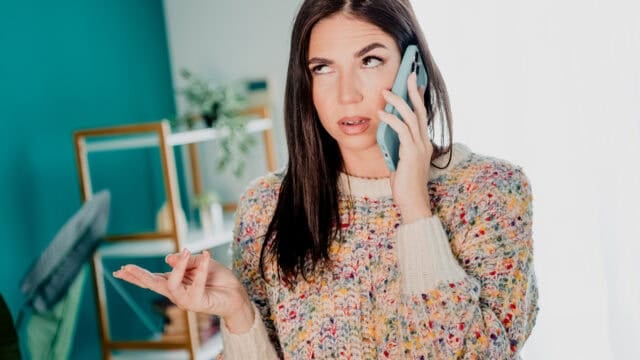A woman wearing a multicolored knit sweater looking frustrated while talking on a smartphone.
