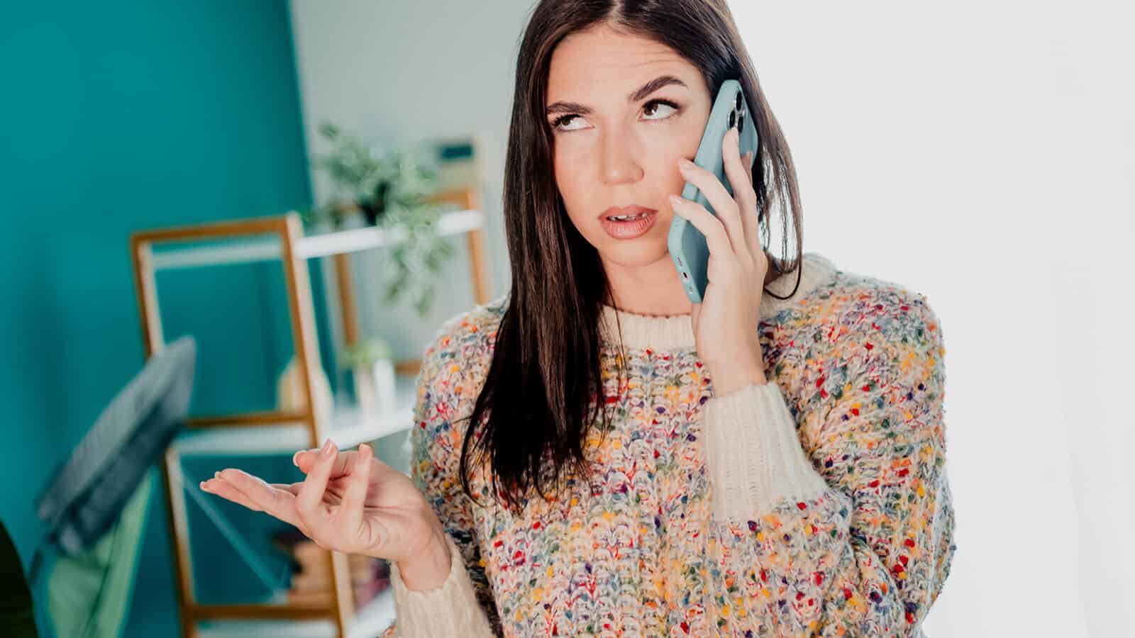 A woman wearing a multicolored knit sweater looking frustrated while talking on a smartphone.