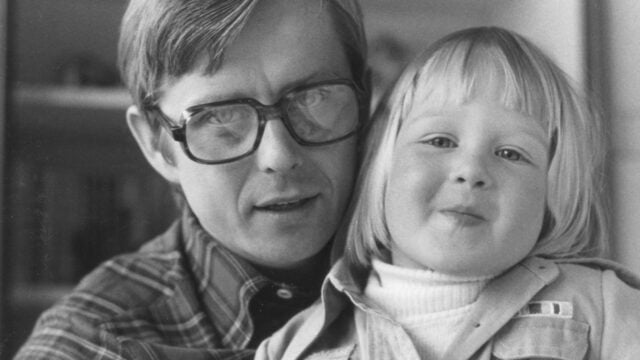 A black and white close-up portrait of a man wearing glasses and a young child leaning against his shoulder.