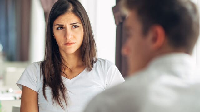 A woman with a concerned expression looks at a person whose back is turned to the camera.
