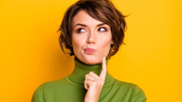 A person in a green turtleneck sweater looking thoughtful with a hand to their chin.
