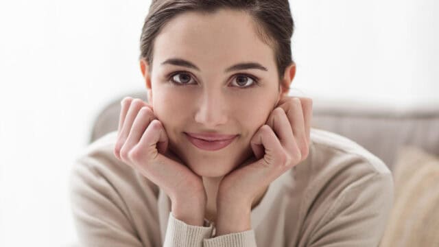 A woman rests her chin on her hands and smiles at the camera.