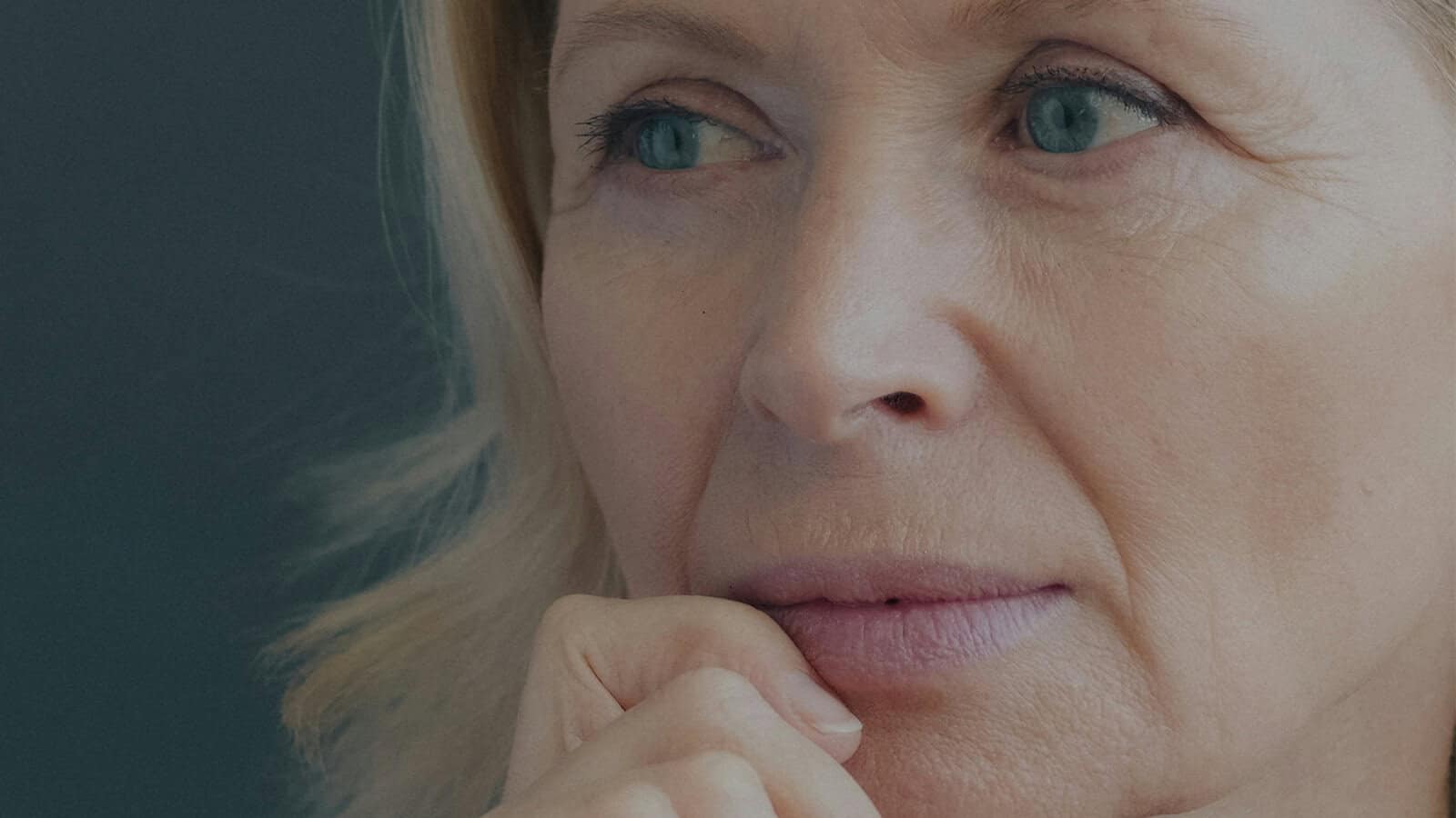 Close-up of a middle-aged woman looking away pensively with her hand held to her chin.