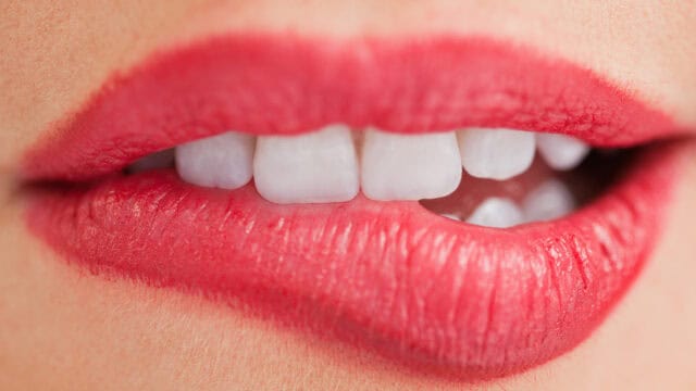 Close-up of teeth biting a lower lip wearing bright red lipstick.