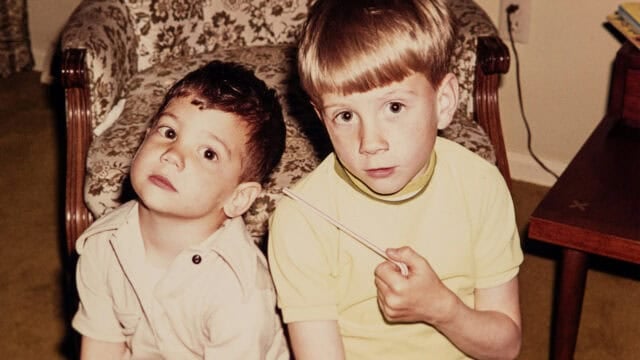 Two young boys sitting side by side, with one holding a drinking straw.
