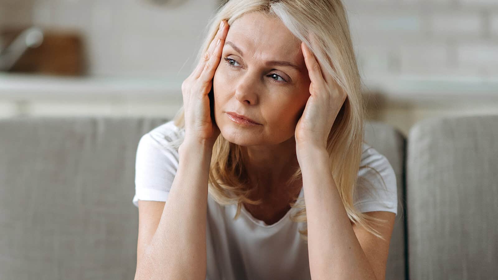 A woman sits with her hands pressed against her temples, appearing stressed or in pain.