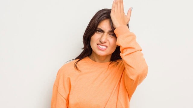 A woman in an orange long-sleeved shirt looking frustrated while slapping her forehead with her hand.