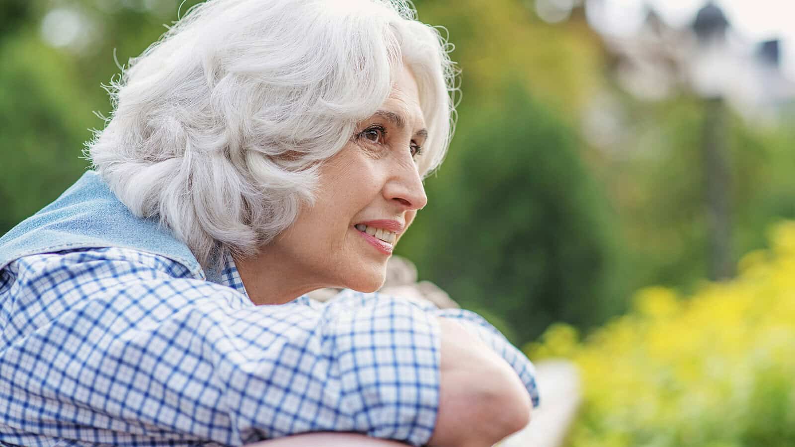 An older woman with white hair looking off into the distance while leaning on a railing.