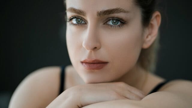 A close-up portrait of a woman resting her chin on her hands.