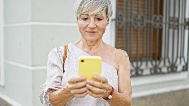 A woman looking down at a yellow smartphone.