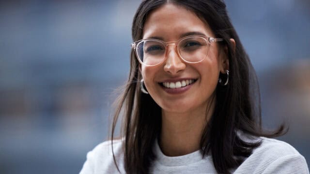 A smiling woman with dark hair wearing clear-framed glasses.