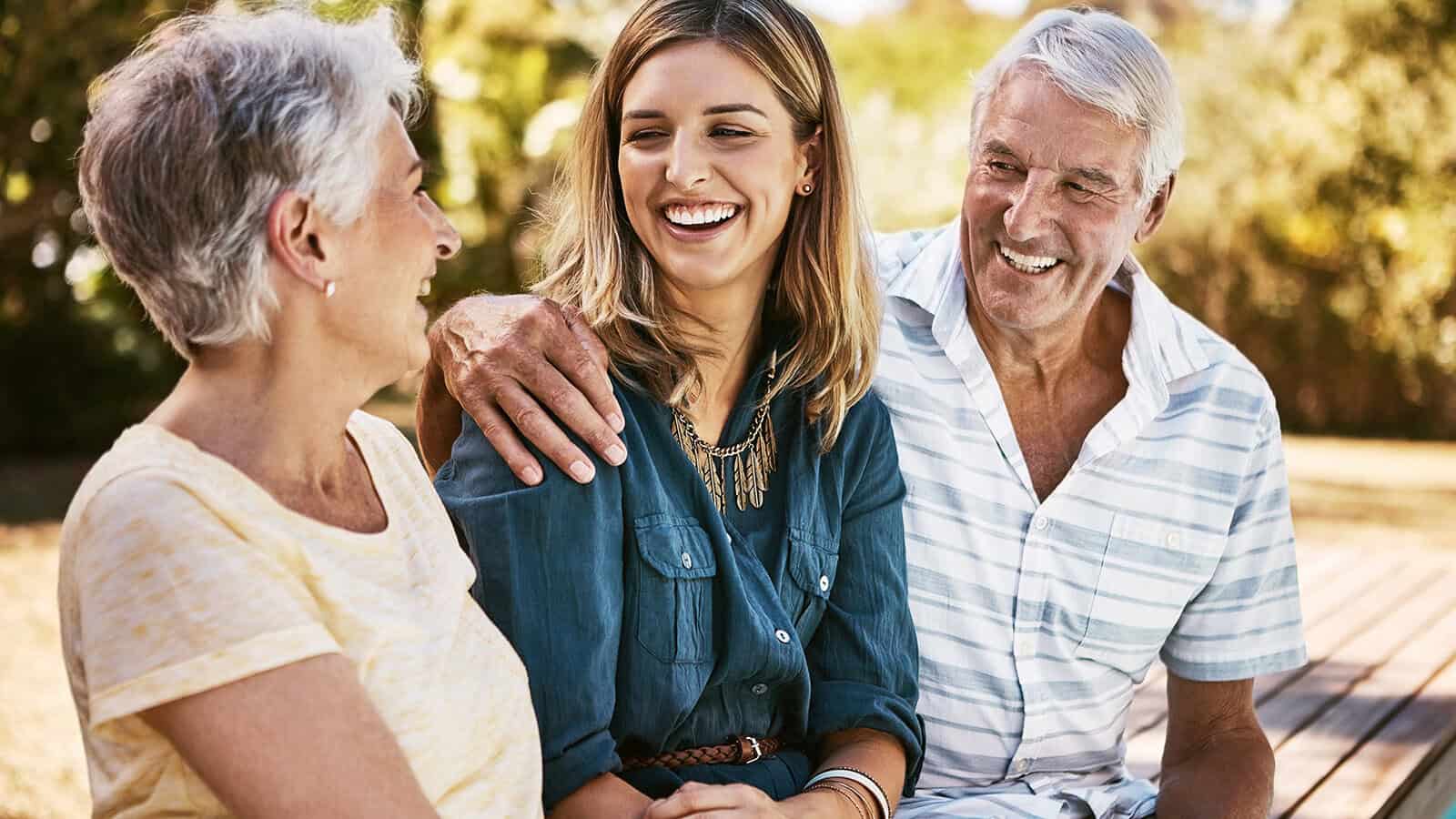 An older woman, a younger woman, and an older man laughing together outdoors.