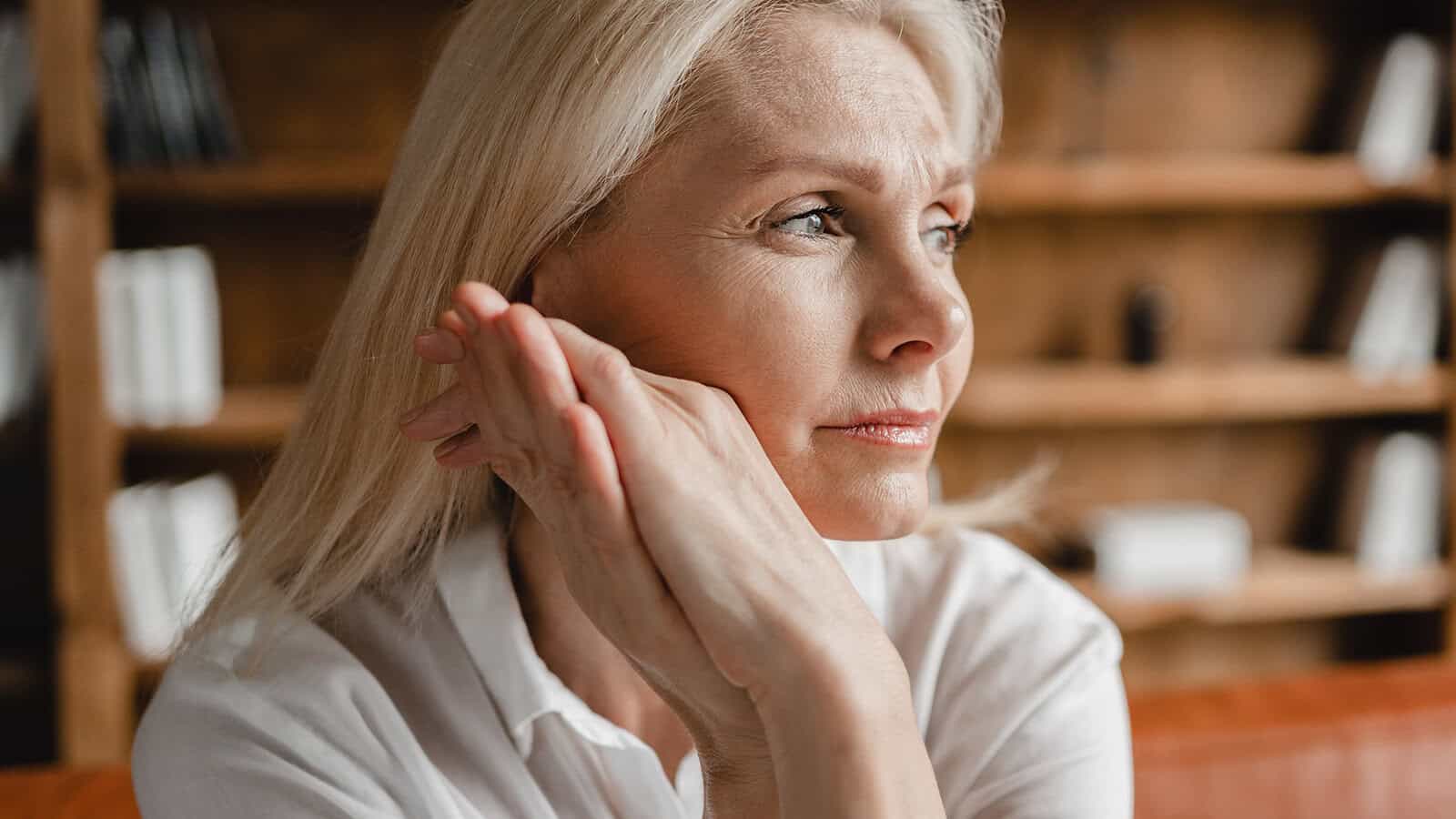 A middle-aged woman with blonde hair resting her chin on her clasped hands while looking away.