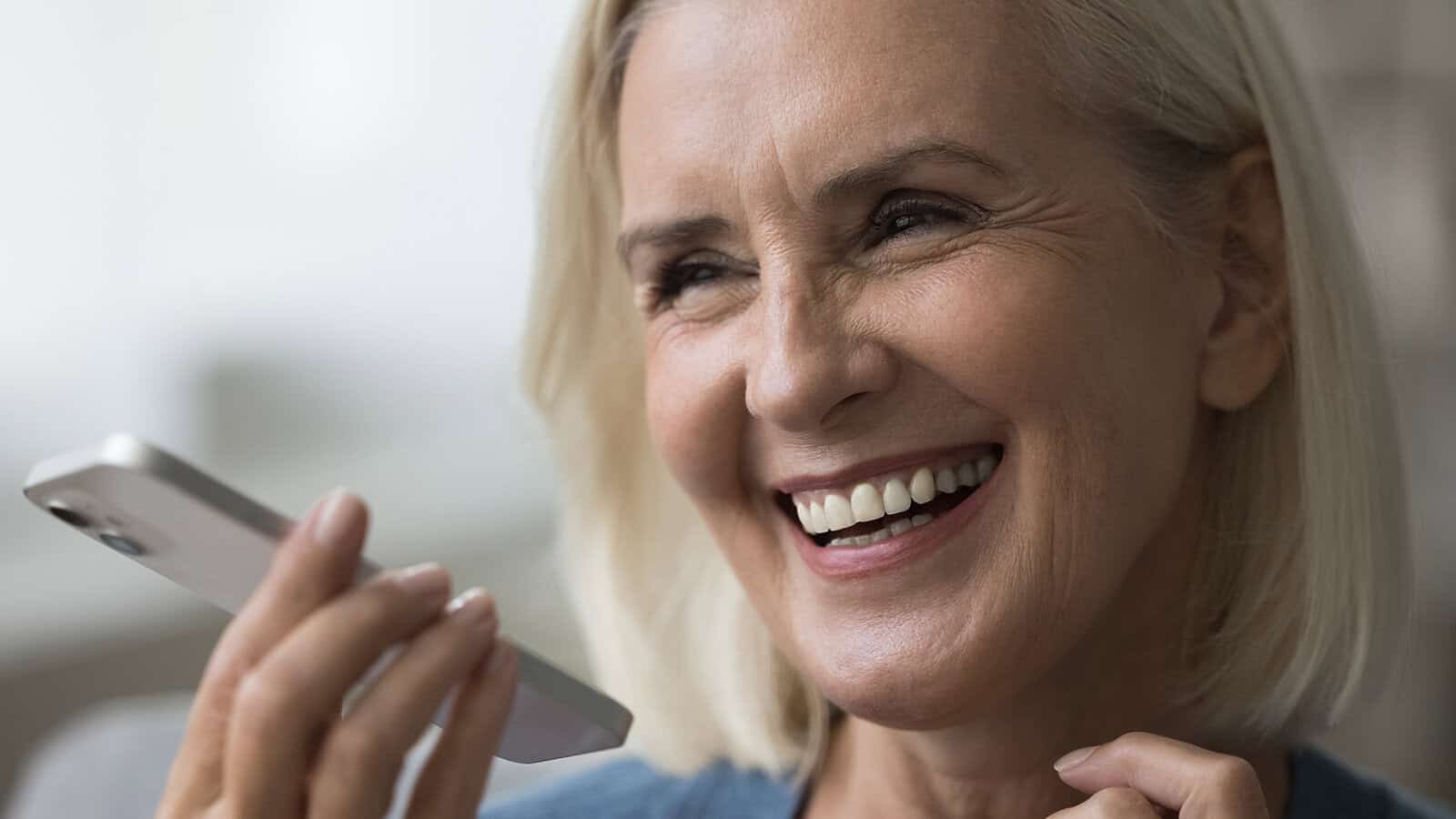 A smiling woman holding a smartphone to her mouth to record a voice message.