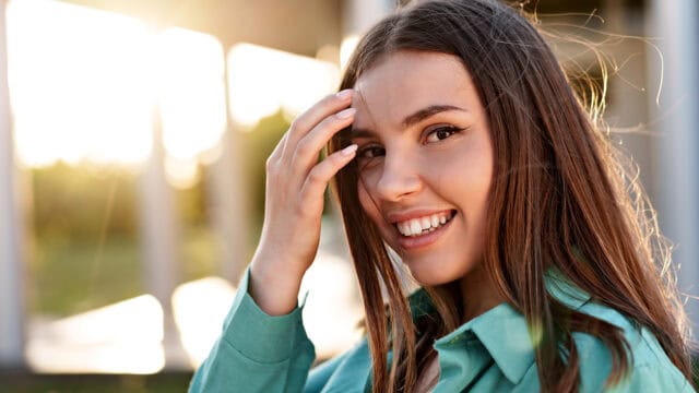 A young woman with long hair smiling as she touches her hair.