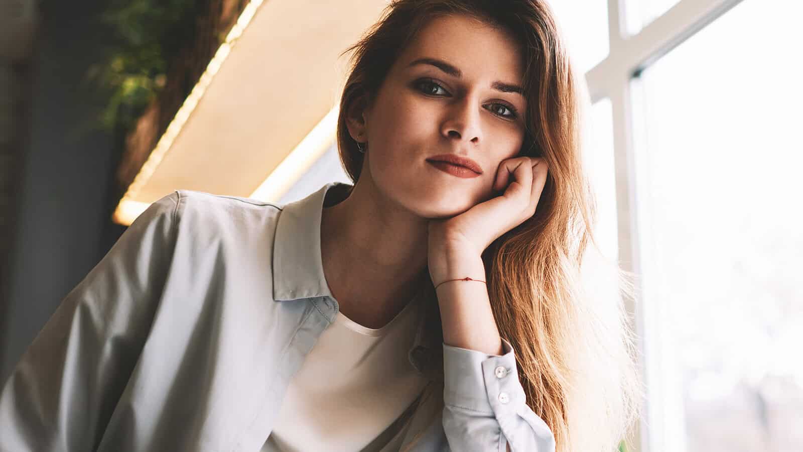 A woman sitting at a table with her chin resting on her hand, looking toward the camera.