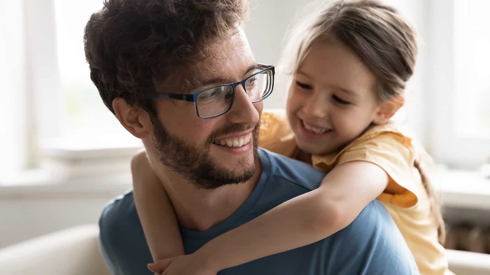 A young girl smiling while giving her father a piggyback ride.