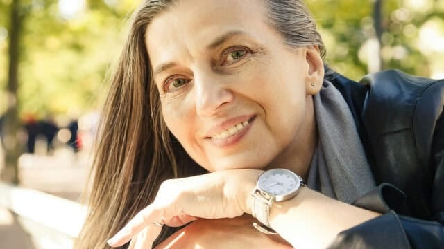 A smiling woman with long hair resting her chin on her hand, wearing a wristwatch.