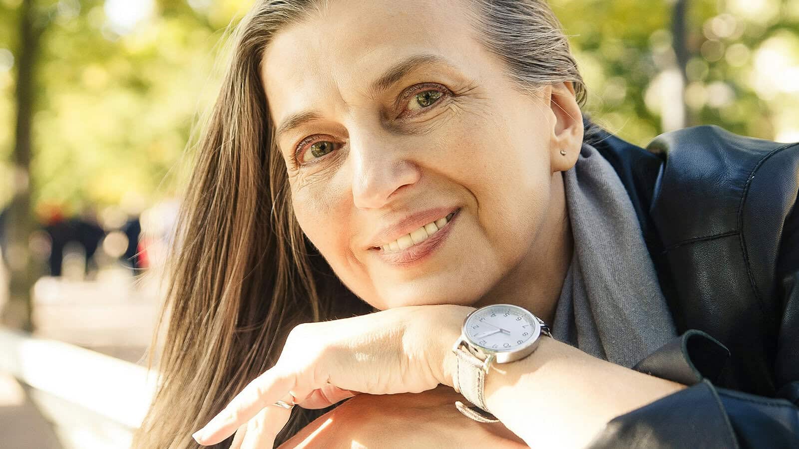 A smiling woman with long hair resting her chin on her hand, wearing a wristwatch.